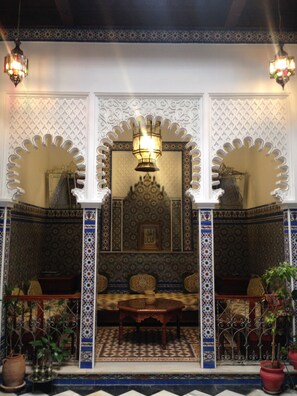 Un interior tradicional marroquí con arcos ornamentales, azulejos estampados y una zona de estar central.