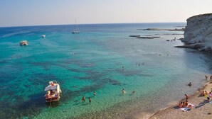 A coastal area with clear turquoise waters, a sandy beach, and rocky formations. - Ayhan Otel (Cesme)