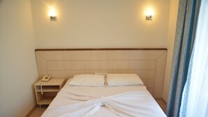 A neatly made bed with white linens and towels, a bedside table with a telephone, and two wall-mounted light fixtures. - Ayhan Otel (Cesme)