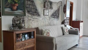 A living room with a beige sofa, a wooden cabinet, and a stone wall accent. - Ayhan Otel (Cesme)
