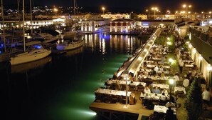 A marina at night with boats docked, a covered dining area, and a building with a dome roof. - Ayhan Otel (Cesme)