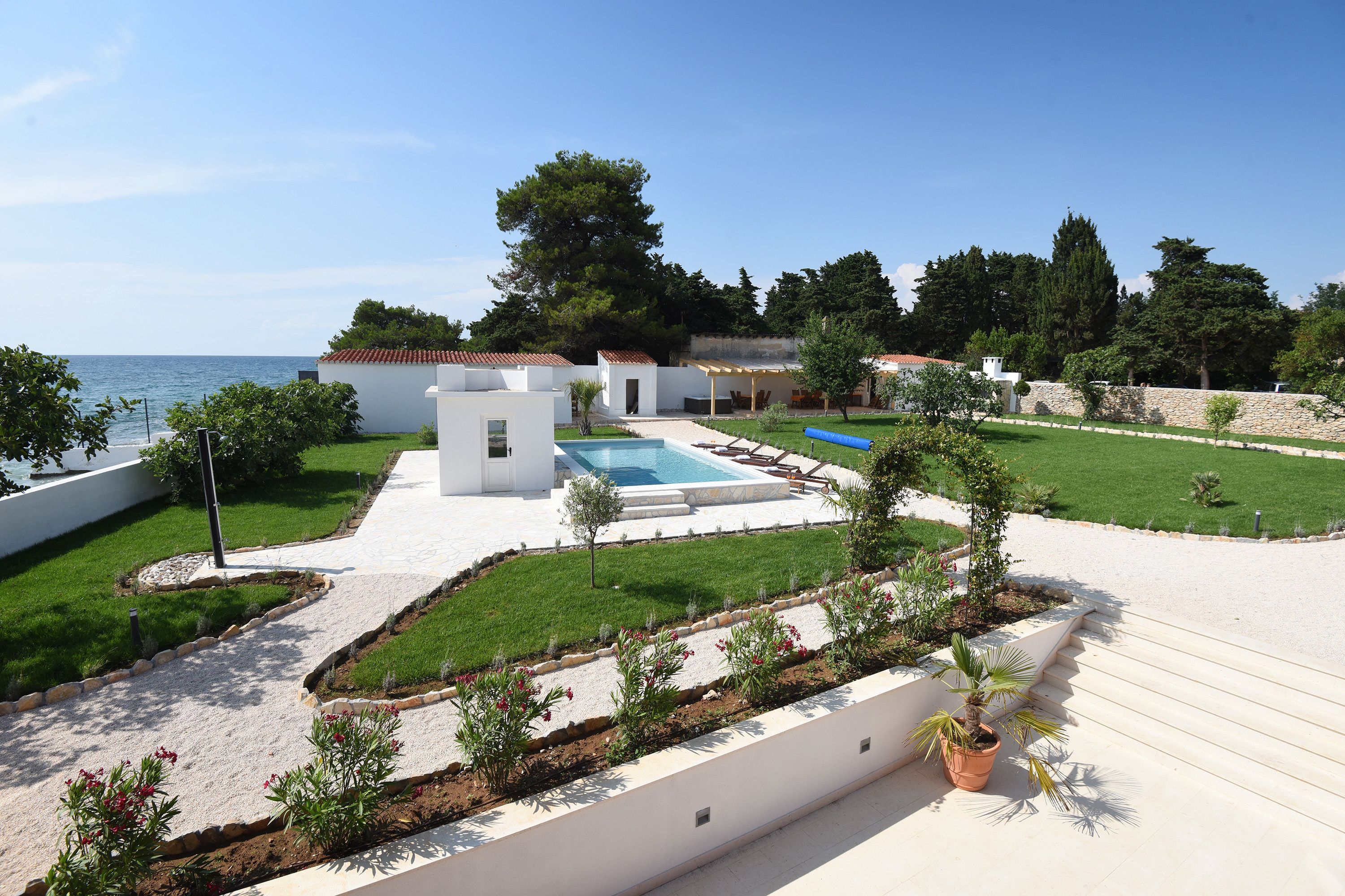 A modern outdoor pool area with a clear view of the sea, surrounded by well-maintained lawns and a stone wall.