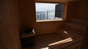 Un sauna con paredes y bancos de madera, una ventana que da al mar y una pequeña mesa con objetos encima.