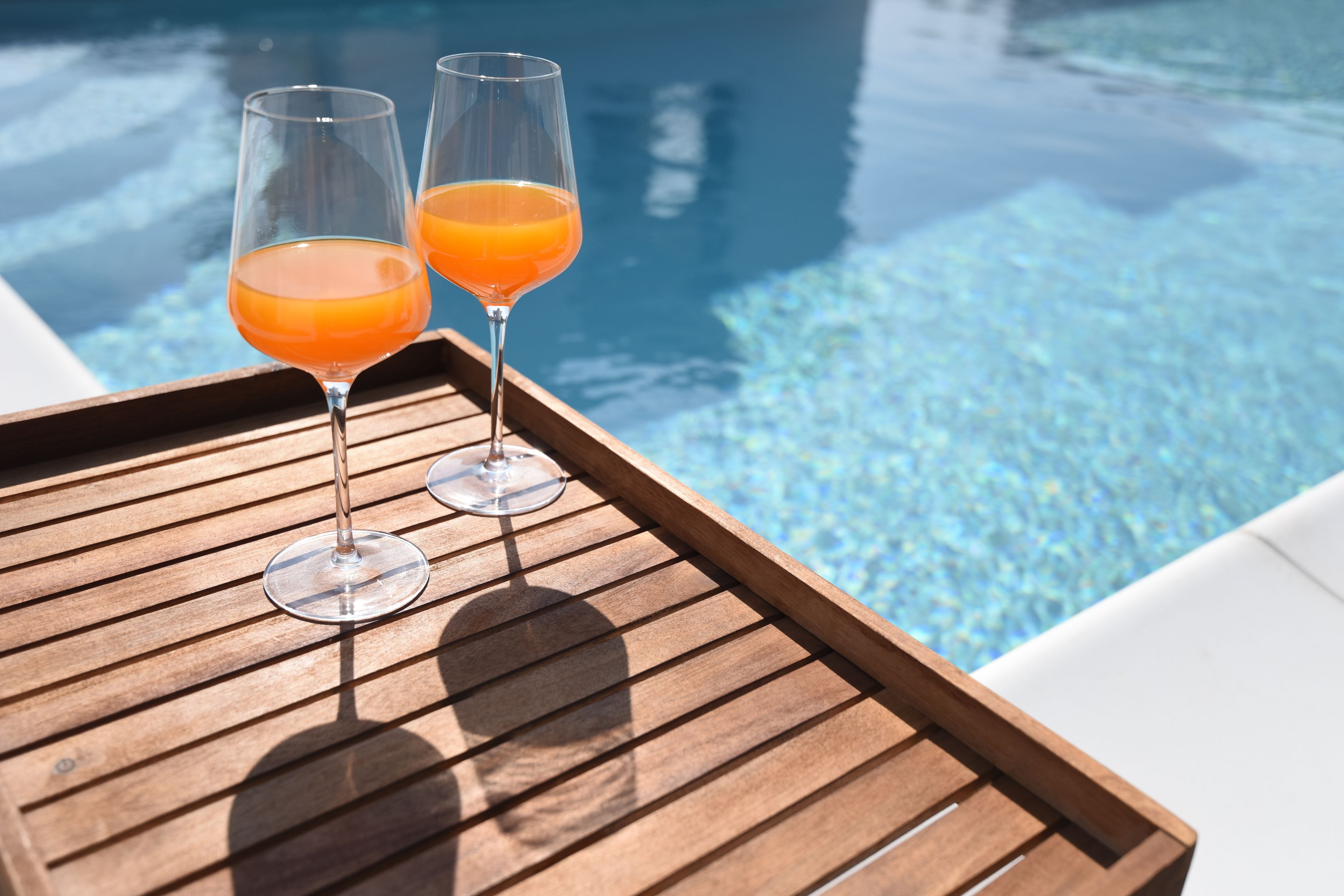 Dos vasos de jugo de naranja sobre una bandeja de madera junto a una piscina.