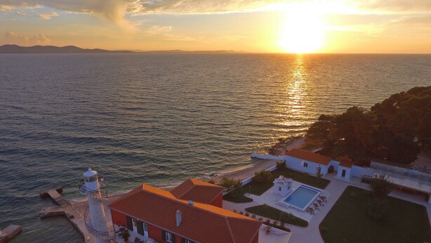 Una propiedad costera con un faro, piscina y vistas al mar al atardecer.