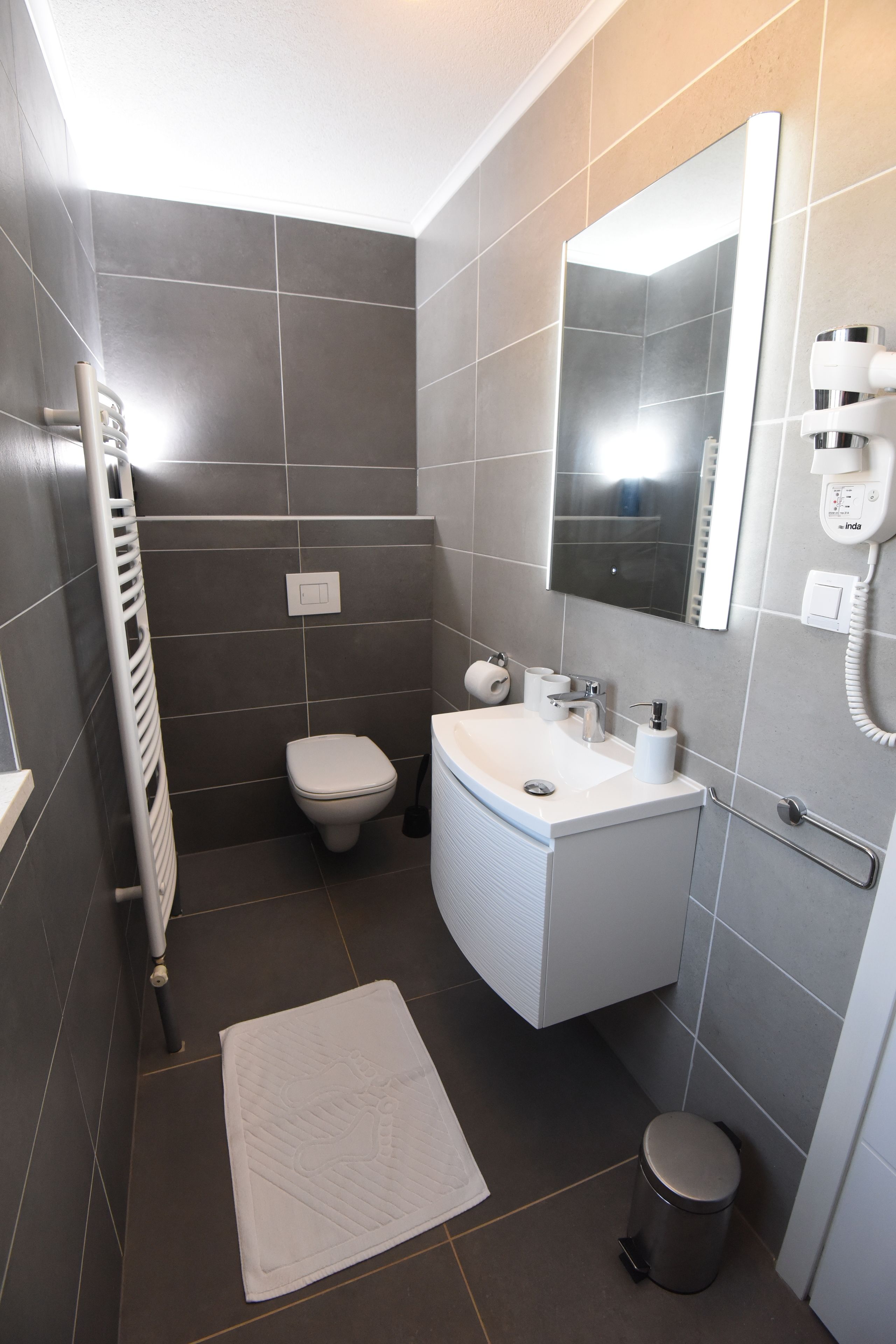 Une petite salle de bain comprenant des toilettes, un lavabo, un miroir et une petite poubelle.