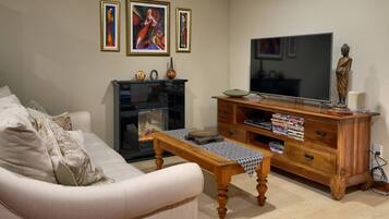 A living room with a sofa, a wooden coffee table, a fireplace, a TV, and a cabinet with DVDs.