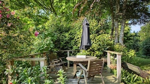 Eine Holzterrasse mit einem runden Tisch und Stühlen, umgeben von üppiger Vegetation und Bäumen.