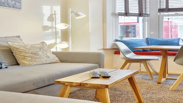 A modern living room with a sofa, a wooden coffee table, and a dining area with a chair and table. - Stylish self contained patio Garden Apartment in London’s fashionable SW6 (Fulham)