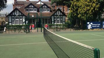 A tennis court with a net, surrounded by a fence, and a building with a sign for Bishops Park Tennis Café in the background.