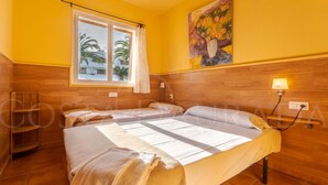 Une chambre avec un lit, une fenêtre avec des rideaux, un tableau au mur et une tête de lit en bois.