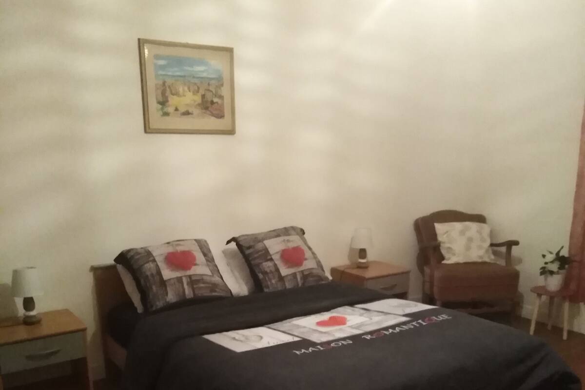 Un dormitorio con una cama, dos mesitas de noche, una silla, una lámpara y un cuadro en la pared.