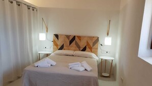 A hotel room with a bed, two bedside tables, a headboard with a geometric pattern, and a window with curtains. - Renovated house in Porto Saler (FORMENTERA)