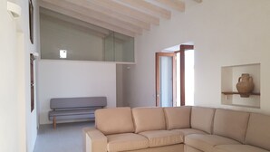 A modern living room with a beige sectional sofa, a grey bench, and a wooden ceiling. - Renovated house in Porto Saler (FORMENTERA)