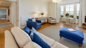 Ein geräumiges Wohnzimmer mit einer Couch, einem Hocker und einem Essbereich mit Tisch und Stühlen.