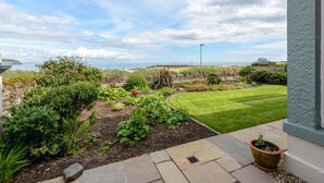 Ein Garten mit verschiedenen Pflanzen und einer Rasenfläche, der zu einem Blick aufs Meer führt.