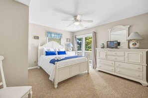 A bedroom with a white bed, a ceiling fan, a dresser, and a window with curtains.