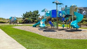 Ein Spielplatz mit mehreren Rutschen und Klettergerüsten, umgeben von einem gepflegten Rasen und blauem Himmel.