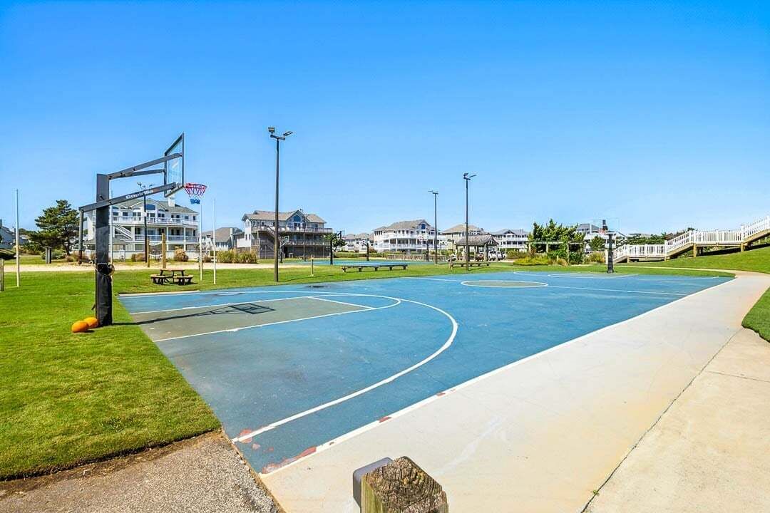 A basketball court with a clear blue surface, surrounded by a grassy area and a walking path.