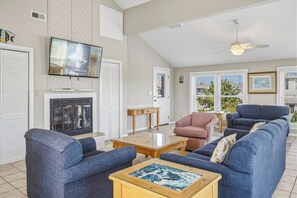 A living room with a fireplace, a television mounted on the wall, and a ceiling fan. - The Finish Line | 320 ft from the beach | Hot Tub, Community Pool | Corolla (Corolla)
