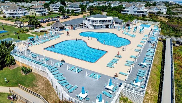 Ein großer Poolbereich mit mehreren Schwimmbecken, Liegestühlen und einer überdachten Terrasse.