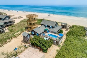 Una proprietà fronte spiaggia con diverse strutture in legno, tra cui una torre a più livelli, una piscina e diversi edifici sul lungomare.