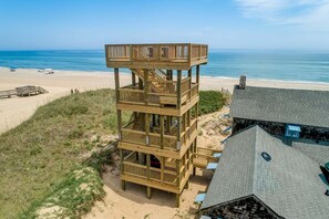 Una struttura in legno a più livelli con balconi, accanto a una spiaggia e a una casa con tetto spiovente.