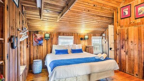 A wooden cabin bedroom with a large bed, two wall-mounted lamps, and a rustic decor. - The Beach House | Oceanfront | Dog Friendly, Private Pool, Hot Tub | Nags Head (Nags Head)