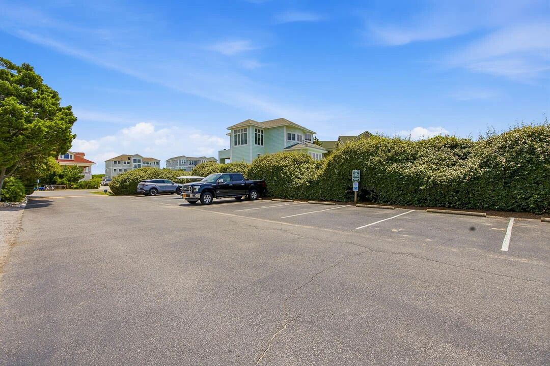 A parking lot with several cars, a hedge, and buildings in the background.