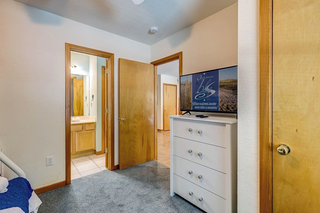 A hotel room with a bed, a dresser, a television, and a bathroom visible through an open door.