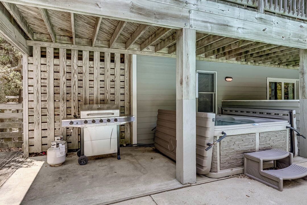 An outdoor patio with a barbecue grill, a hot tub, and a covered seating area.