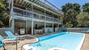 A two-story building with a pool area, including lounge chairs and a barbecue setup.