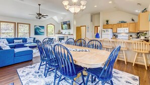 A spacious living room with a large wooden dining table surrounded by blue chairs, a blue sofa, and a chandelier.