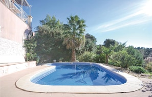 A swimming pool with a curved edge, surrounded by a paved deck and various plants. - Amazing apartment in Les Issambres (Les Issambres)