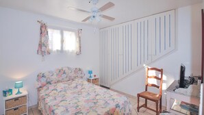 Ein Schlafzimmer mit Bett, Sessel, Schreibtisch und Deckenventilator.