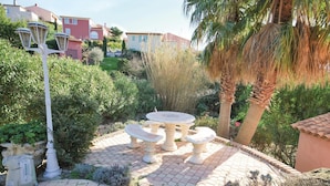 Eine Gartenpatio mit rundem Tisch und Bänken, umgeben von üppiger Vegetation und Palmen.