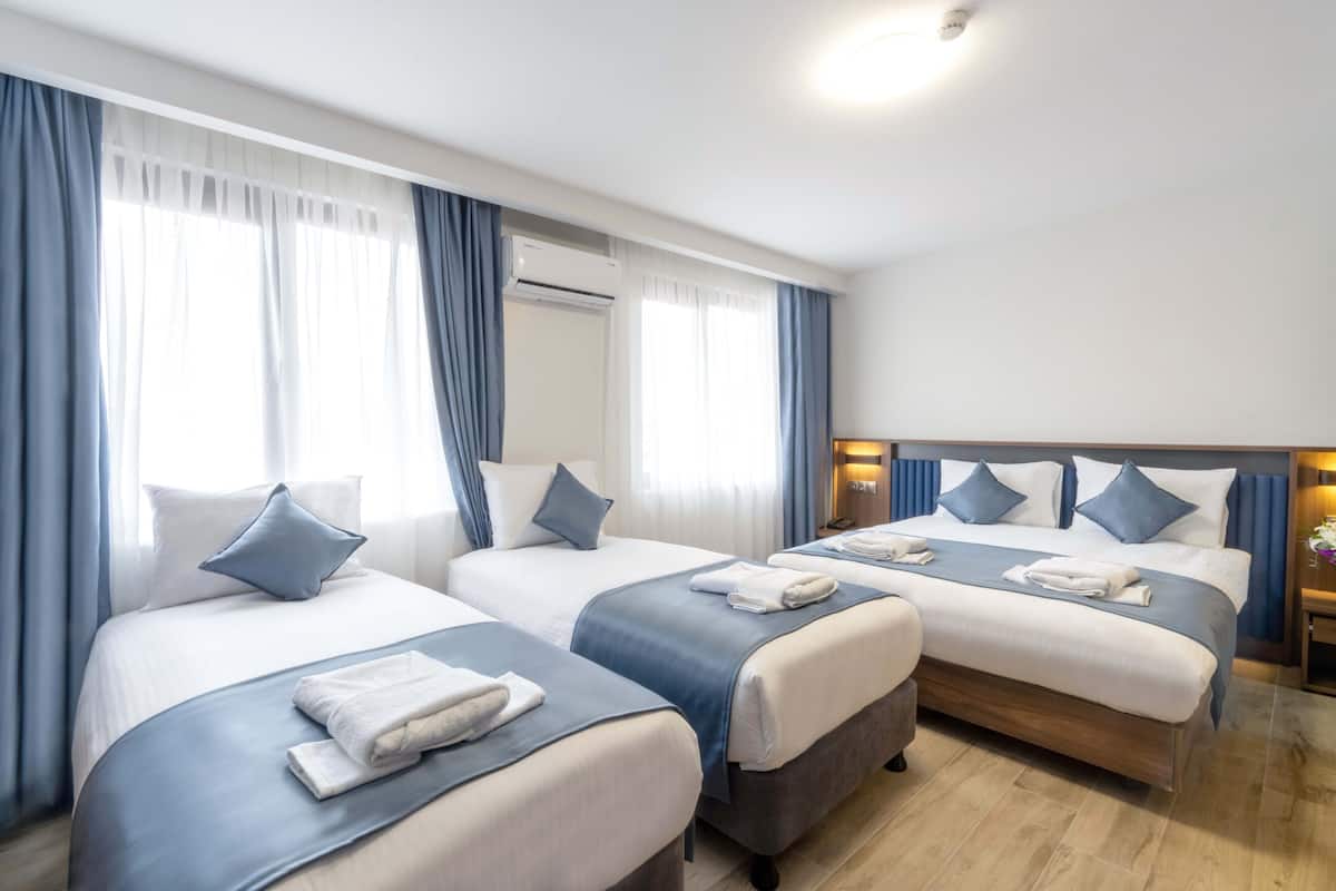 A hotel room with three beds, each with a blue bedspread and white pillows, and a wooden headboard.