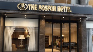 Exterior de The Bosfor Hotel, amb façana moderna, grans finestres de vidre i una entrada destacada amb escales cap a la porta.