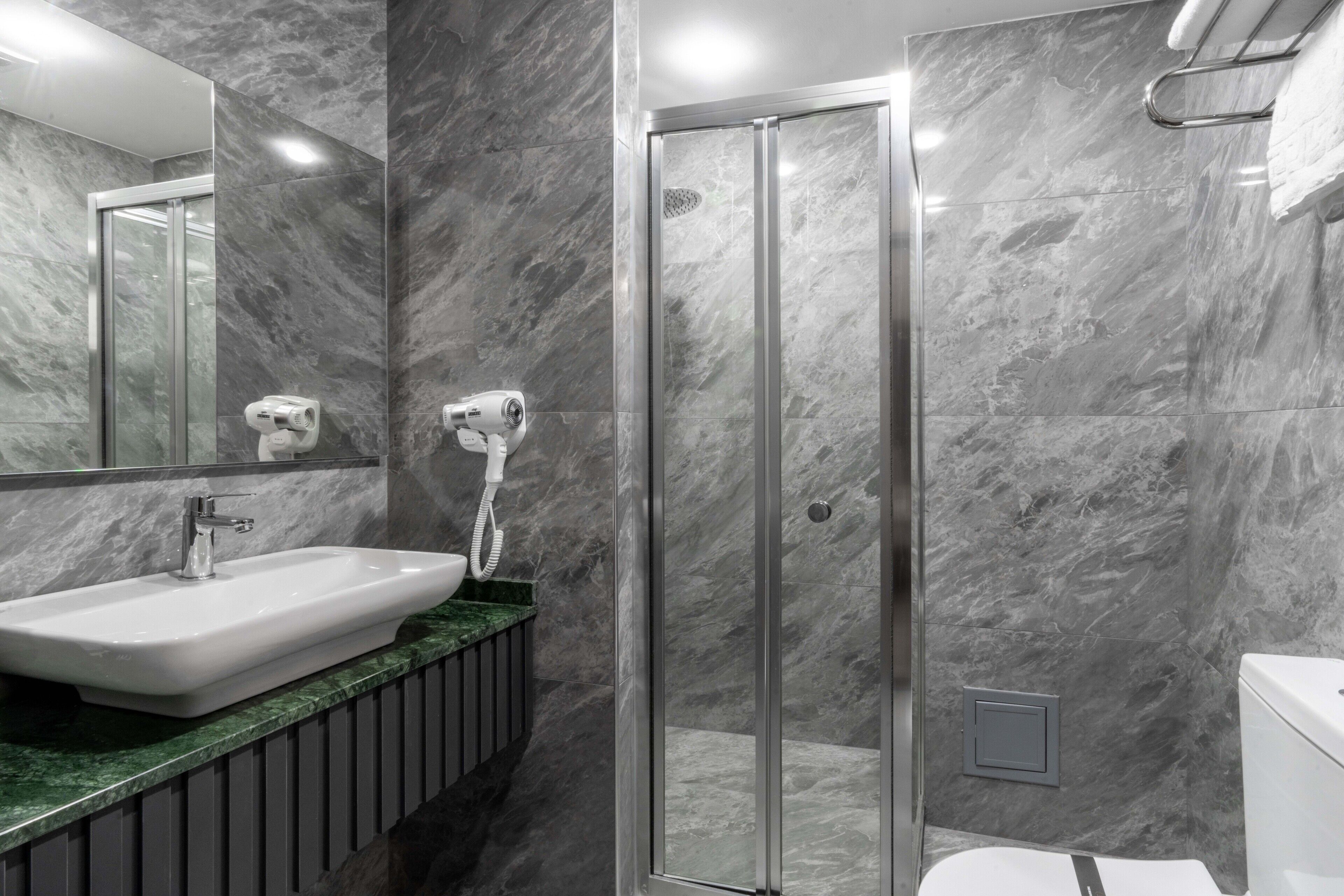 A modern bathroom with a marble sink, a glass shower enclosure, and a toilet.