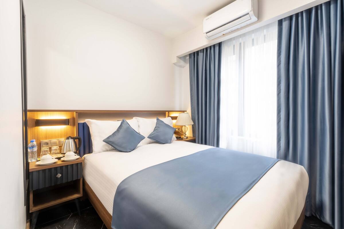 A hotel room with a large bed, a nightstand with a lamp, a water bottle, and a coffee pot.