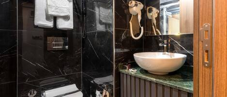 Un baño moderno con tocador de mármol negro, un lavabo blanco y una ducha con cabezal de ducha de mano.