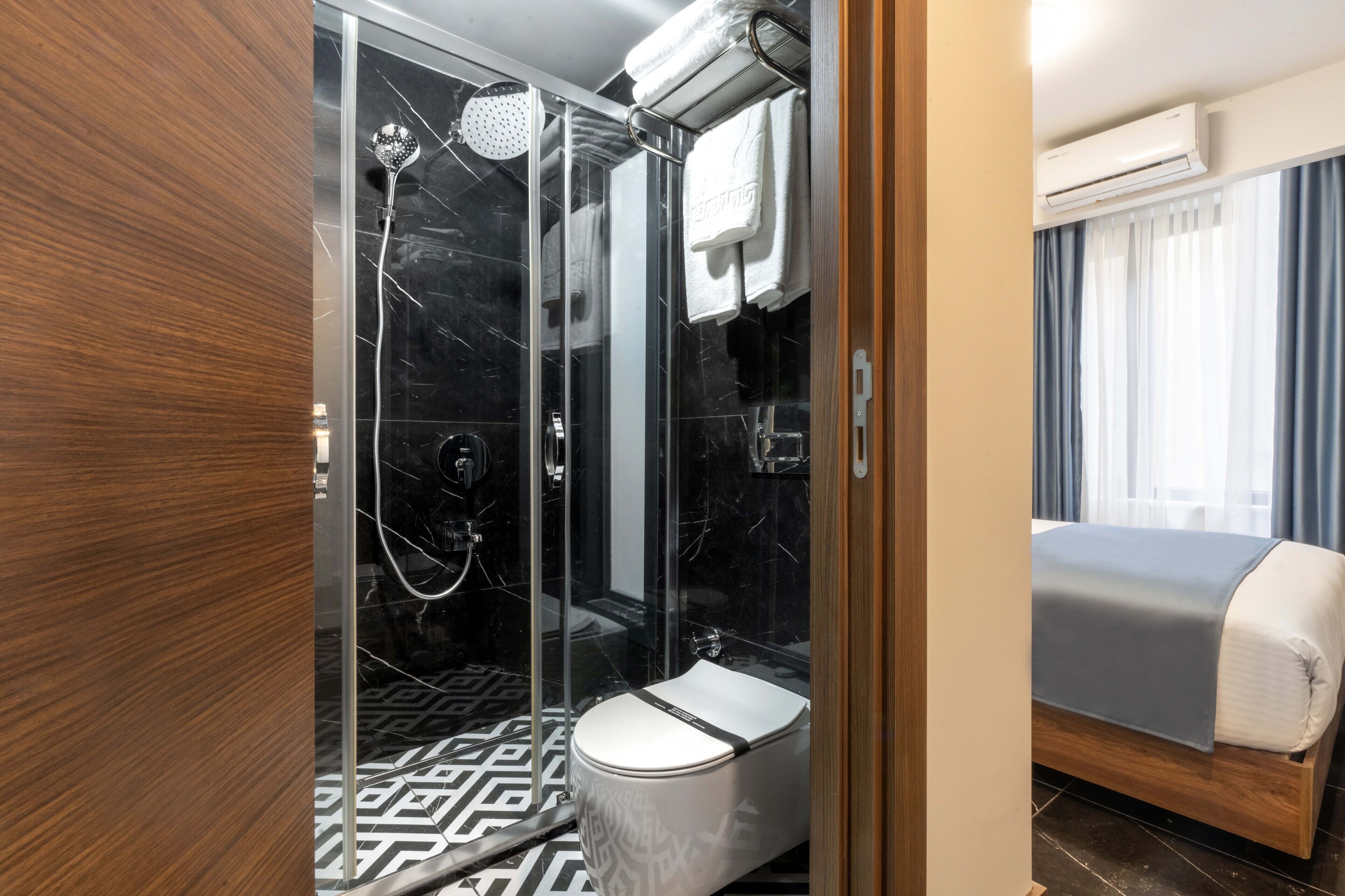 Un baño moderno con ducha de vidrio, inodoro y cama con manta gris.