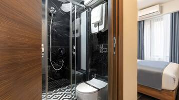 Un baño moderno con ducha de vidrio, inodoro y cama con manta gris.