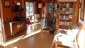 A cozy living room with a fireplace, a bookshelf, and a comfortable seating area. - Cute Cottage - Cooks Beach Bach (Cooks Beach)
