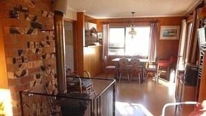 A cozy living room with a fireplace, a dining area, and a kitchen. - Cute Cottage - Cooks Beach Bach (Cooks Beach)