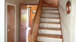 A wooden staircase with a handrail, a door on the left, and a light fixture on the wall. - Cute Cottage - Cooks Beach Bach (Cooks Beach)
