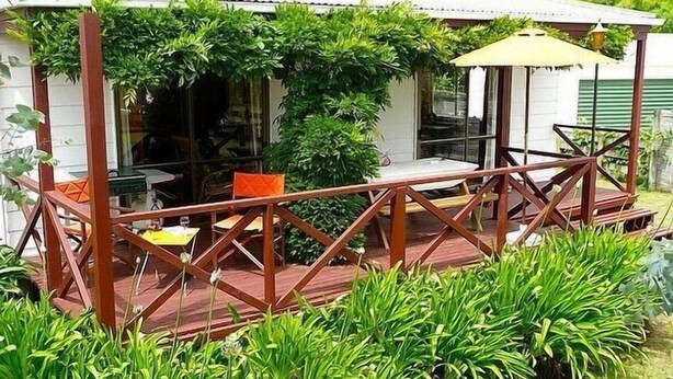 A wooden deck with a railing, surrounded by lush greenery. - Cute Cottage - Cooks Beach Bach (Cooks Beach)