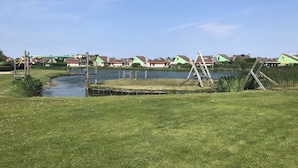 A grassy area with a small pond, a fallen ladder, and houses in the background.