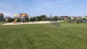 A playground with various play equipment, a grassy field, and houses in the background.
