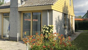 A house with a brick chimney, large windows, and a garden with flowers.